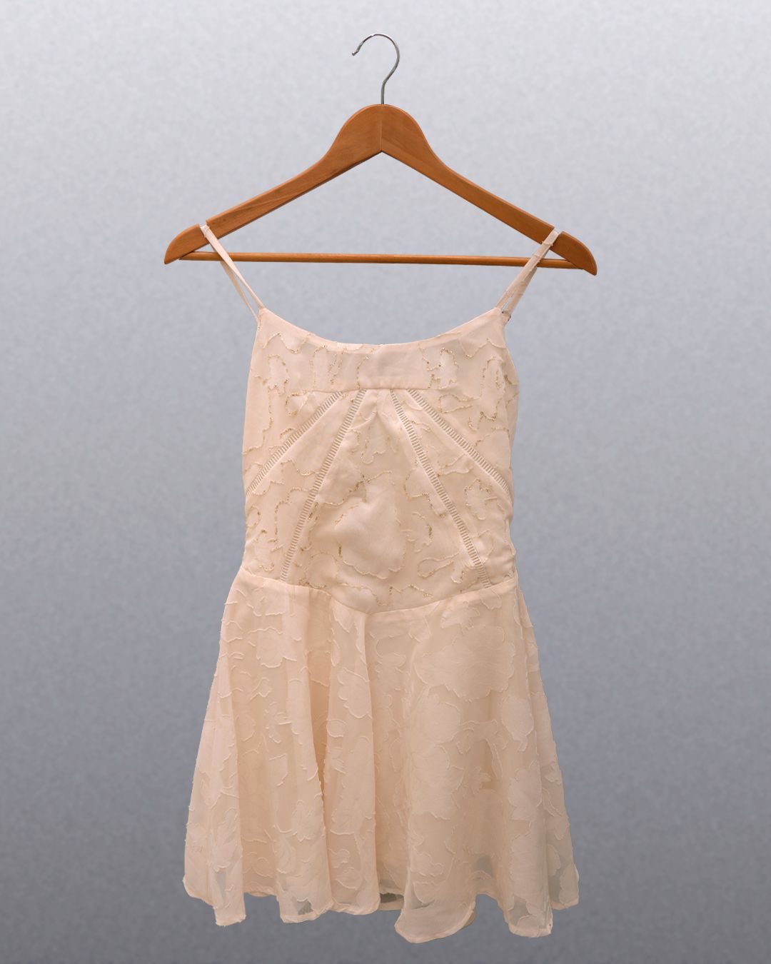 Antes: vestido curto off-white de alcinha, com textura floral, pendurado num cabide de madeira
